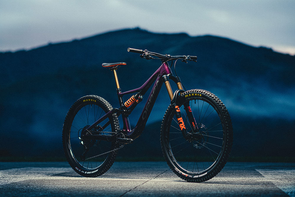 A purple and black Orbea Rallon Mountain bike, with a mountain in the background.