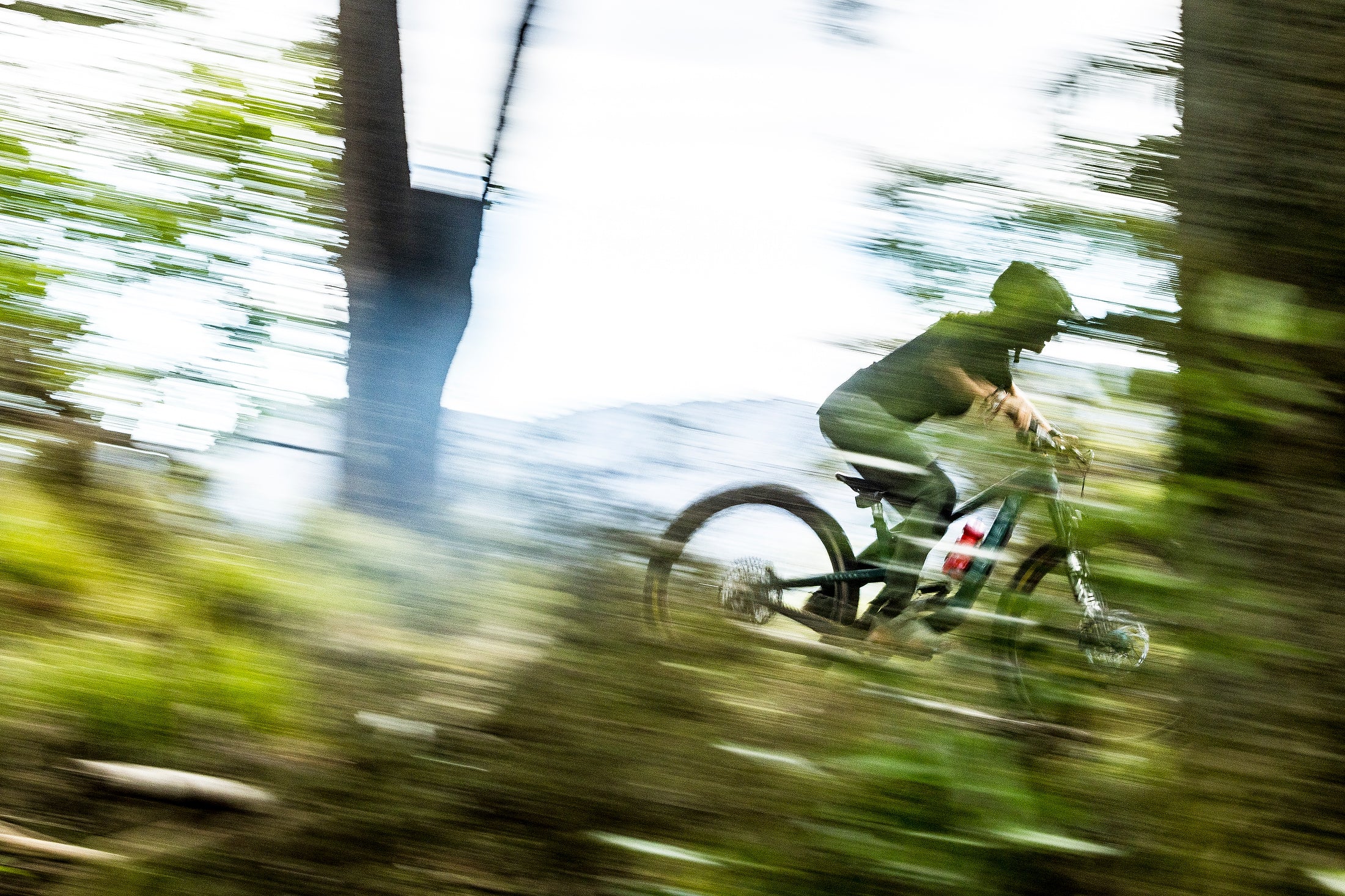 An action shot of a woman riding a Juliana Furtado bike through a lush forest trail, skillfully navigating roots and uneven terrain, showcasing the bike’s agility and performance, available at Contender Bicycles.