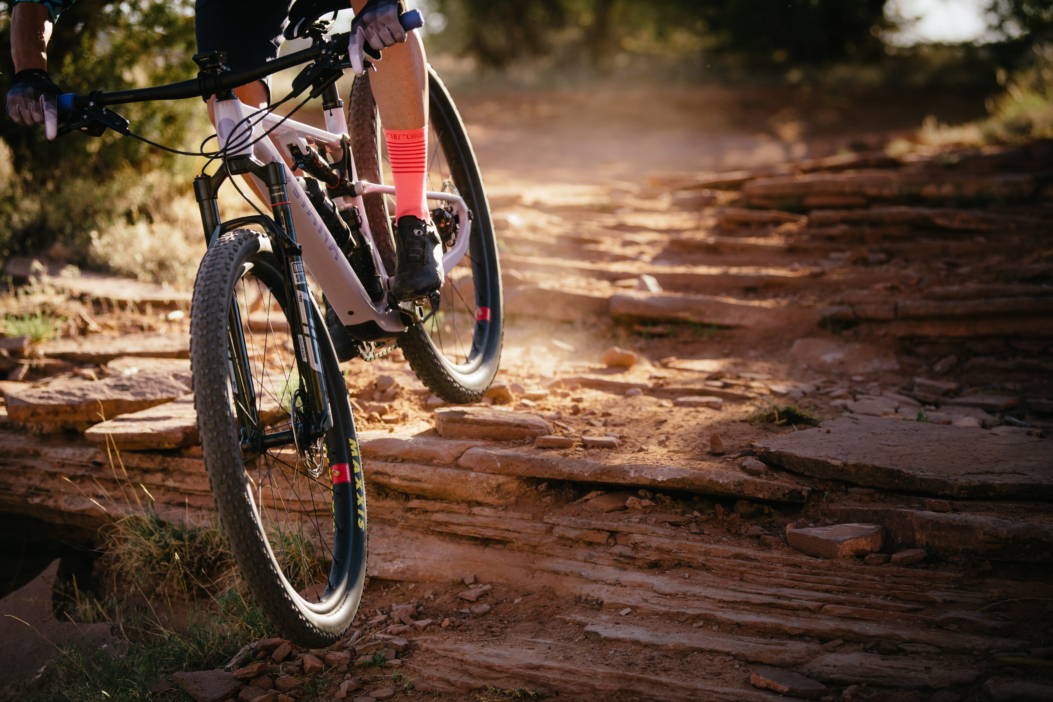 A close-up shot of a Juliana Wilder mountain bike airborne as it leaps off a ledge in the high desert, with rugged terrain and distant desert landscape in the background, showcasing the bike’s agility and performance in challenging environments, available at Contender Bicycles.