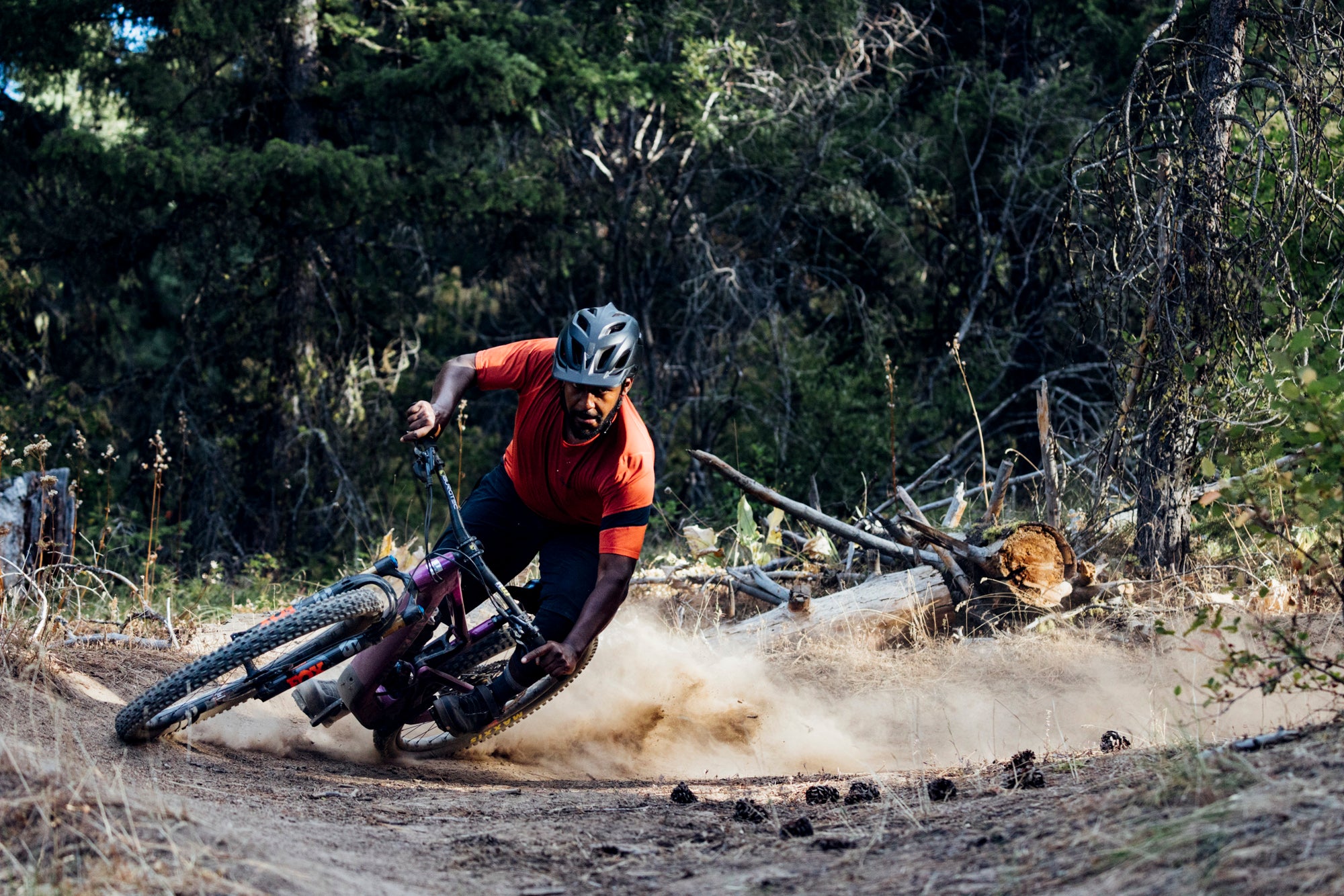 An action shot of a man carving a sharp corner on a Santa Cruz Heckler SL e-bike, kicking up dirt on a rugged trail, with dense trees and natural scenery surrounding him, available at Contender Bicycles.