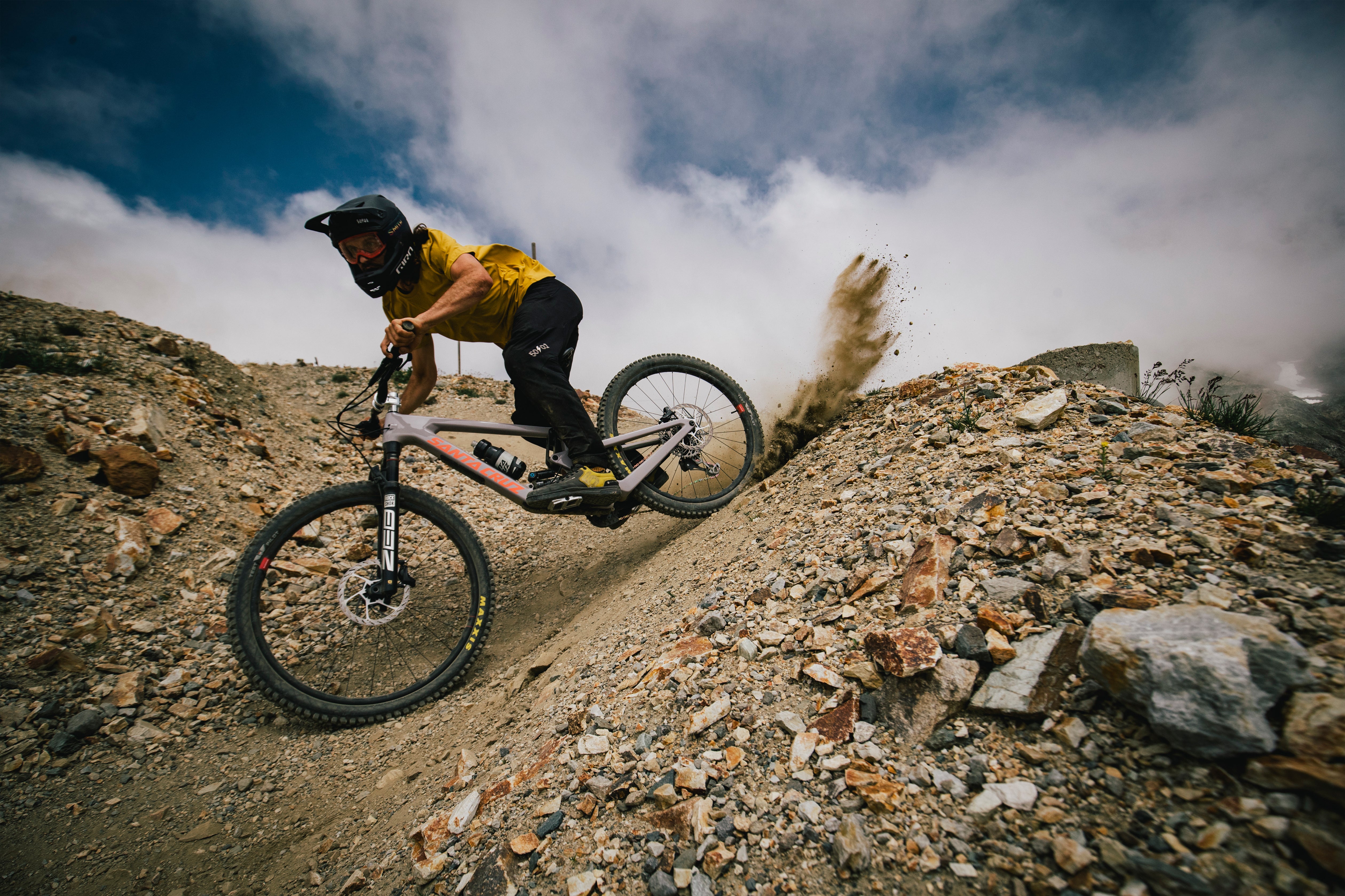 An action shot of a man riding a Santa Cruz Nomad down a rocky mountain trail, navigating through loose rocks and rugged terrain, showcasing the bike's stability and performance in challenging conditions, available to purchase at Contender Bicycles.