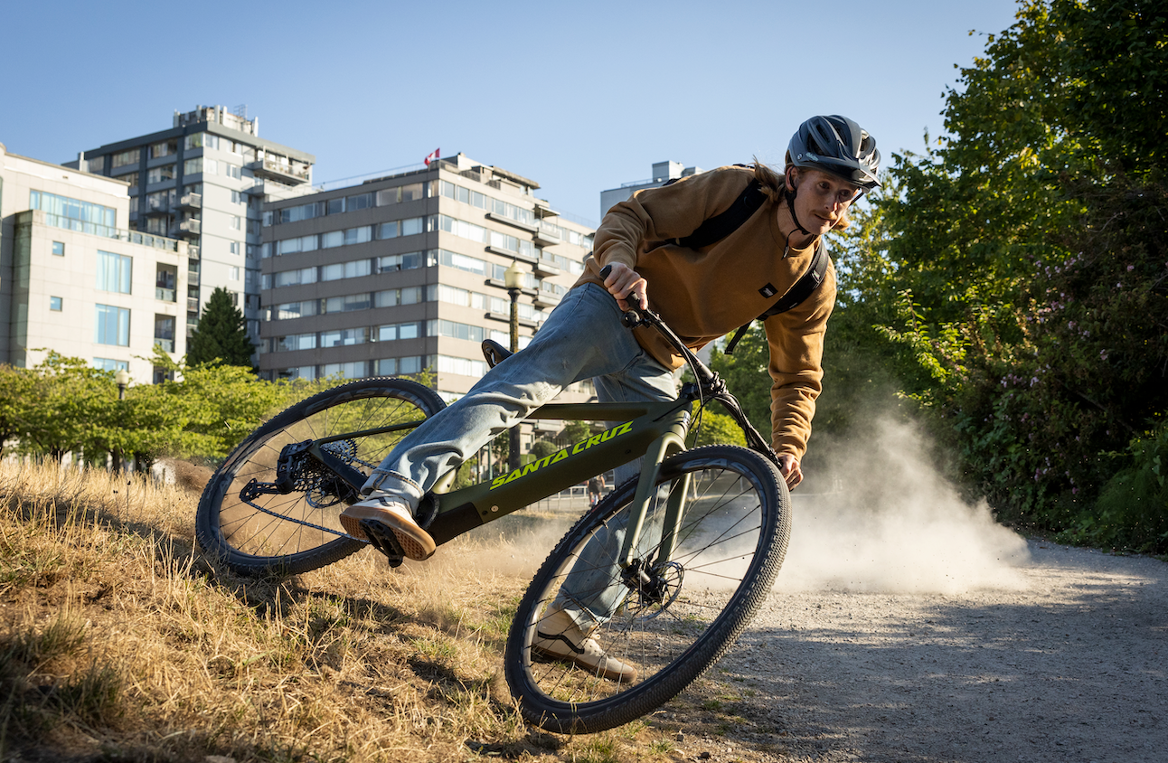 An action shot of a man riding a Santa Cruz Stigmata electric bike along a dirt path with dry, dead grass, showcasing the bike’s agility and performance in rugged terrain, available at Contender Bicycles.