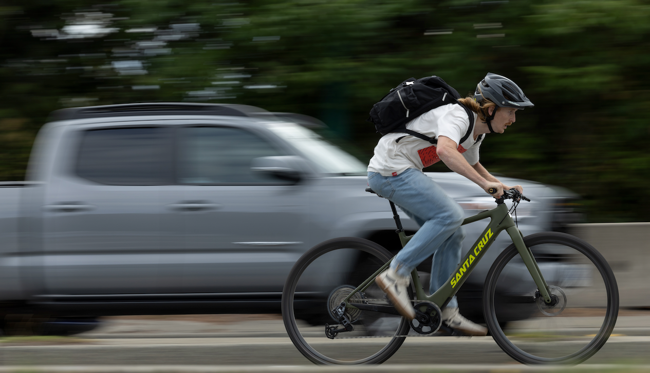 An action shot of a man launching off a jump on a Santa Cruz Stigmata electric bike, soaring through a construction site with scaffolding and machinery in the background, showcasing the bike’s power and agility in an urban landscape, available at Contender Bicycles.