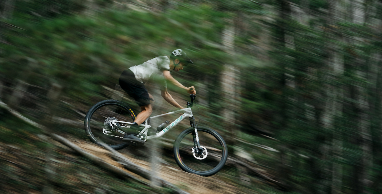 An action shot of a man riding a Santa Cruz Tallboy through a forest trail, navigating loose rocks and uneven terrain, showcasing the bike’s stability and performance in challenging conditions, available at Contender Bicycles.