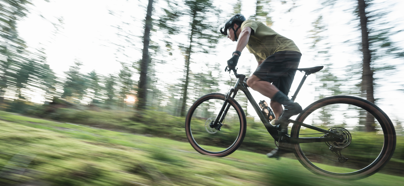 A man is riding the Scott Spark Mountain bike through the forest. 