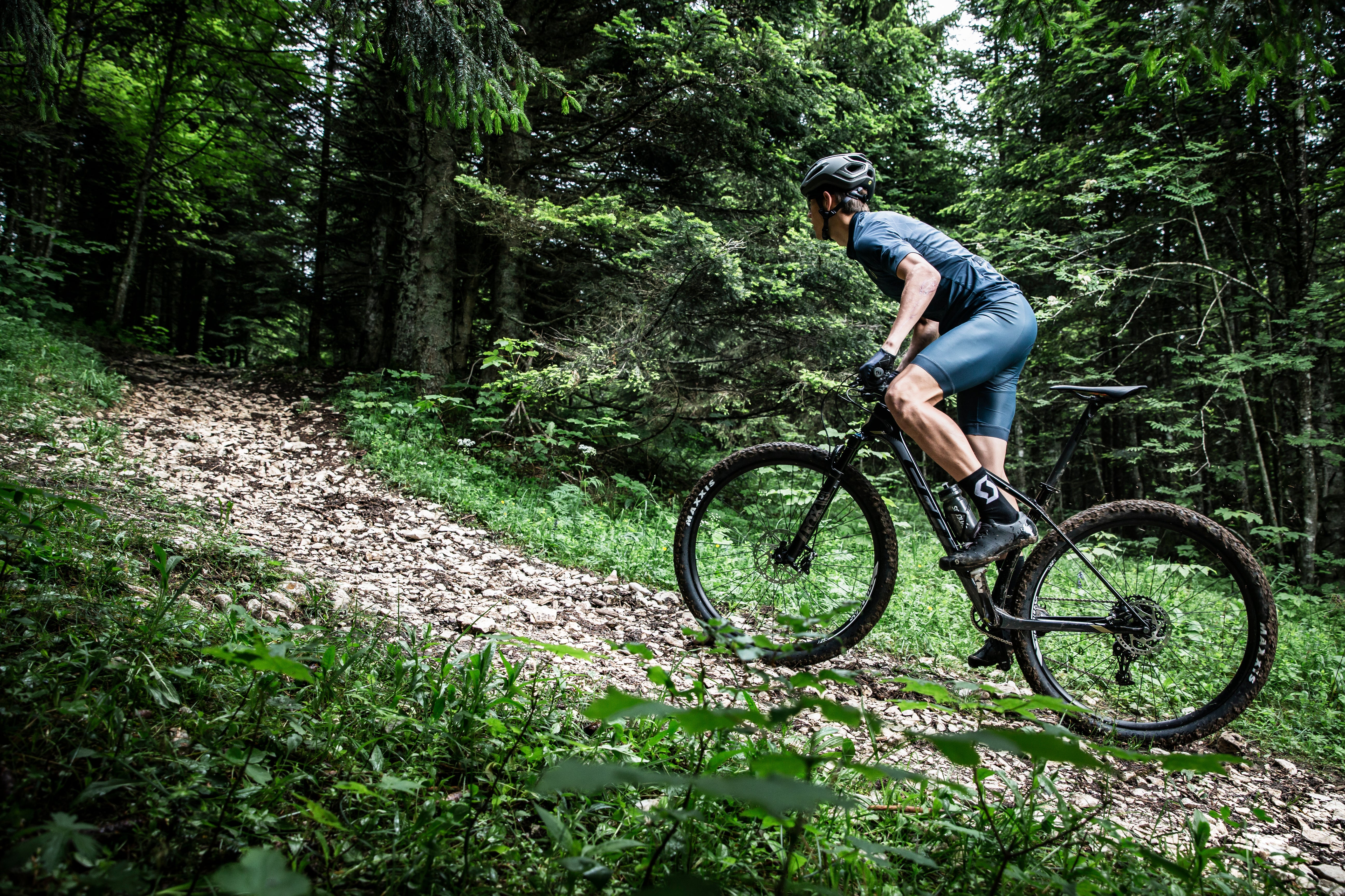 A man riding the Scott Scale mountain bike up a trail in a forest. 