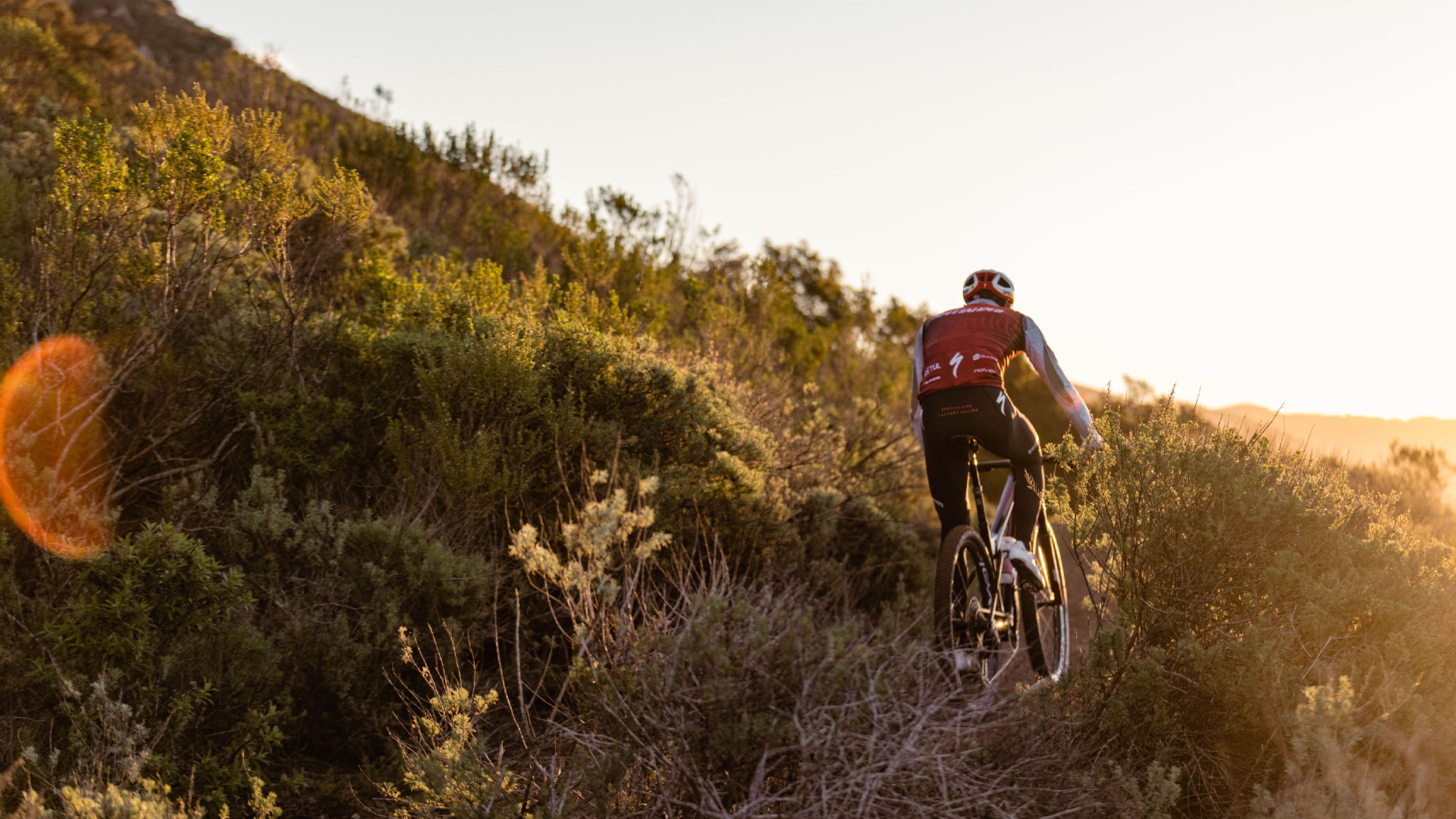 A man riding a Specialized bike in the mountains surrounded by grass during sunset