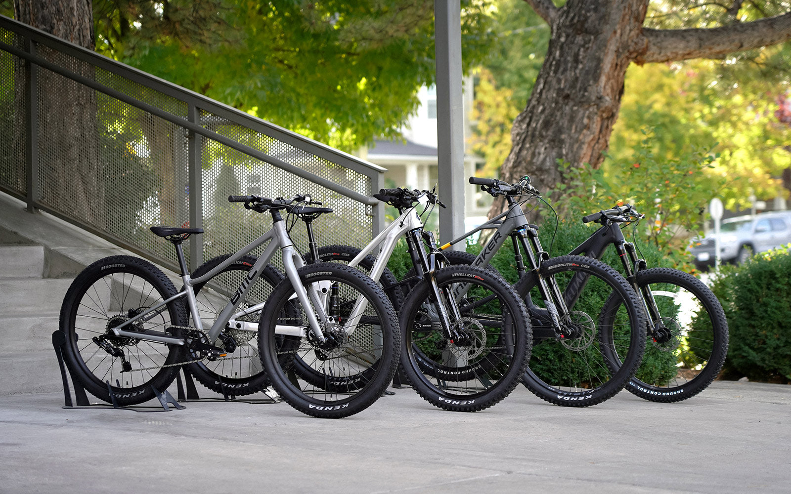 Four kids bikes staged in front of stairs and bushes.