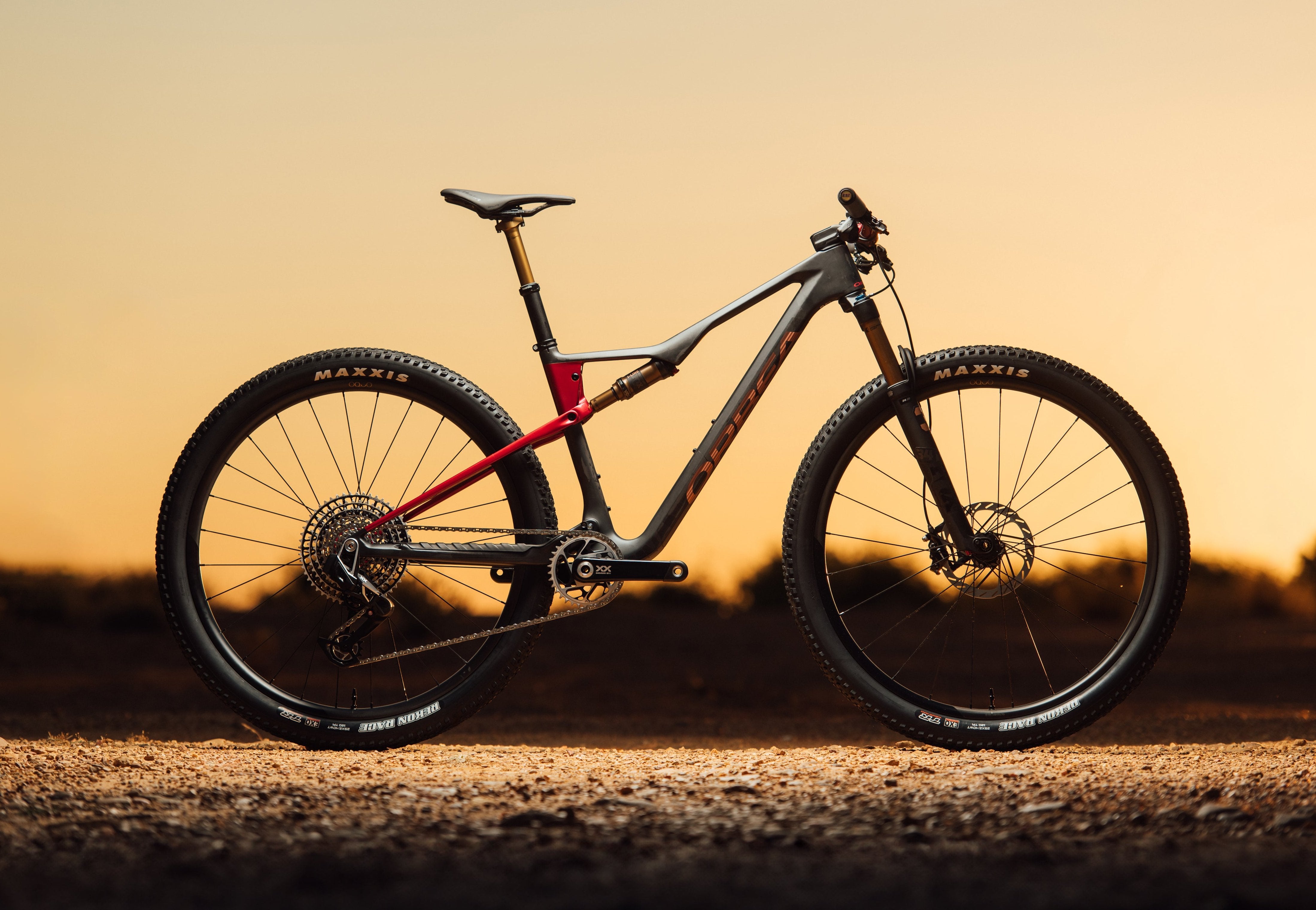 The 2025 Orbea Oiz mountain bike, with gray and red paint, staged against a sunset.