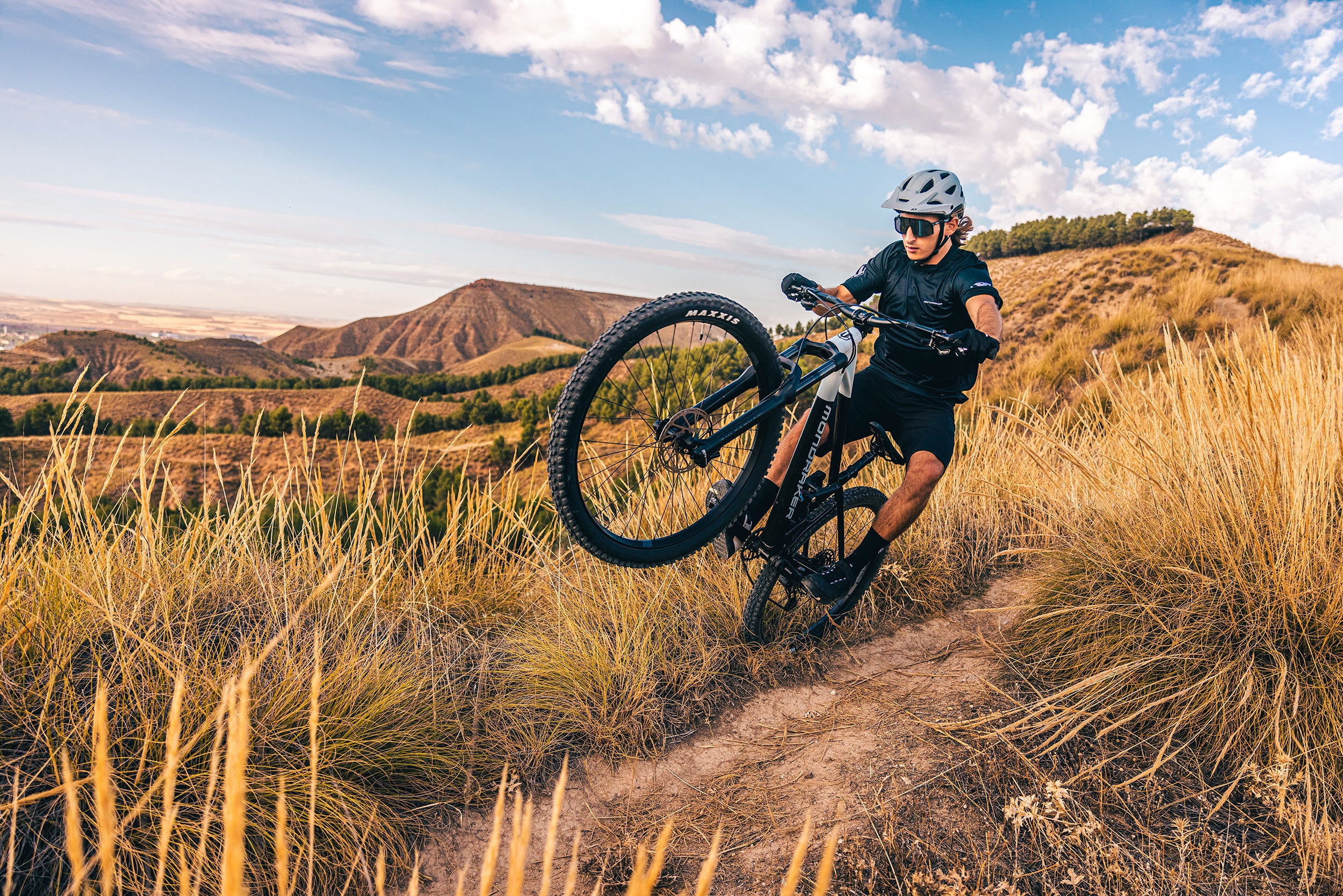 A man doing a wheelie on a Mondraker mountain bike in the mountains