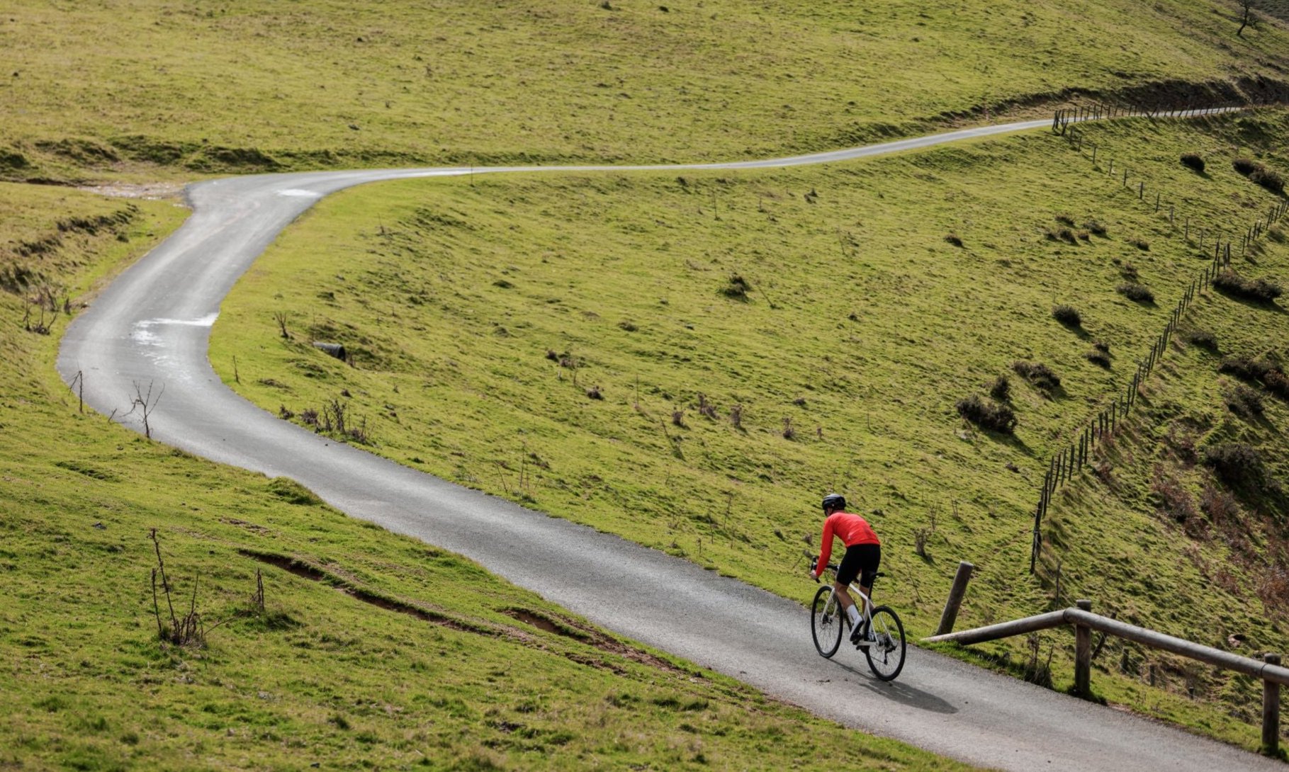 a man in a red shirt riding The Orbea Avant road bike up a grassy hill. 