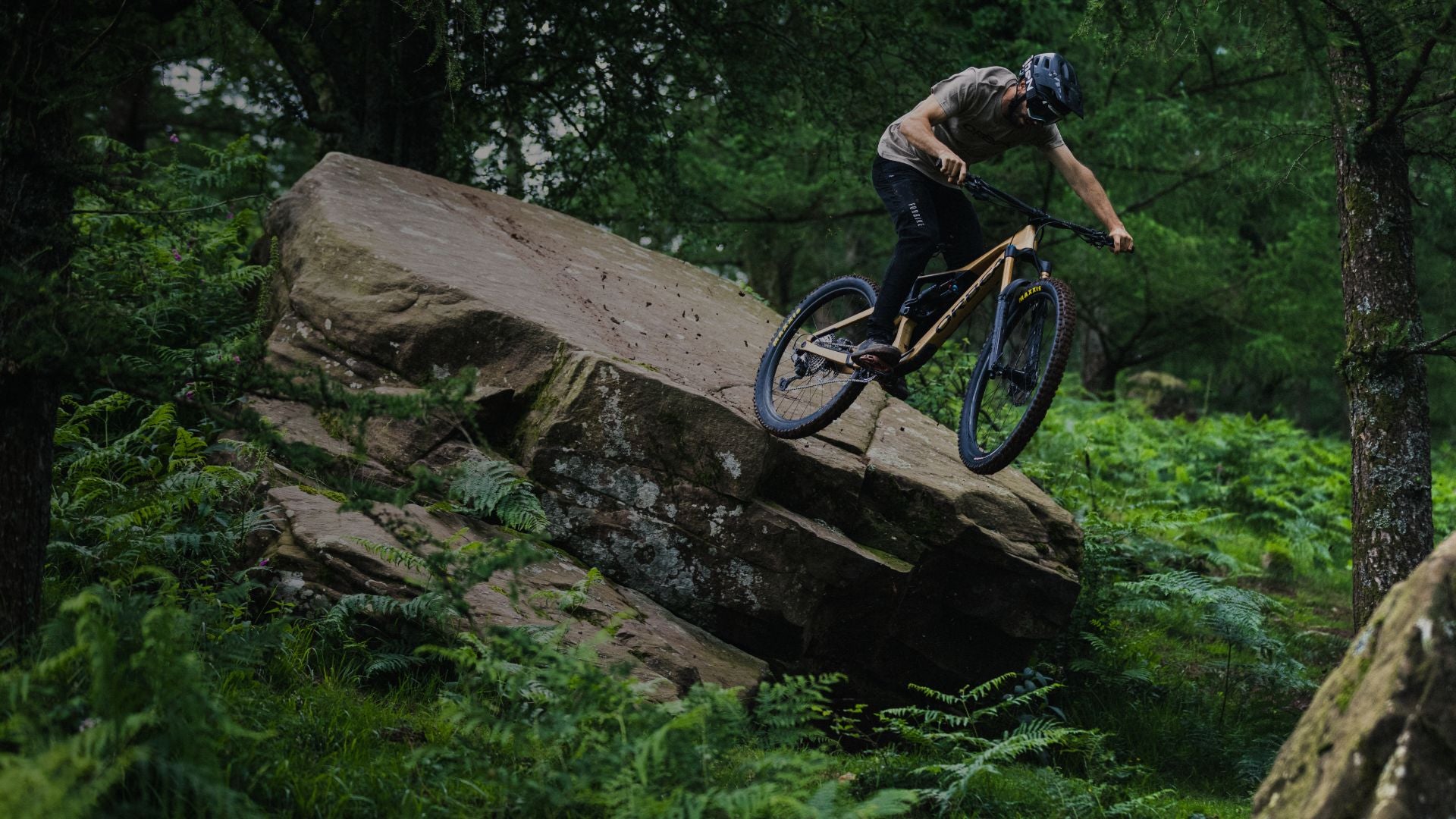 a man in a forest riding an Orbea Rallon mountain bike off a jump. 