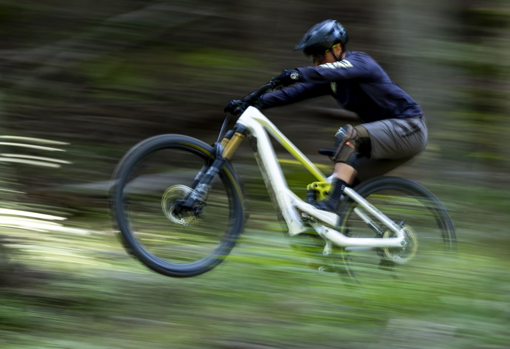 A man riding the Orbea Wild E- mountain bike with white paint. Quickly through a forest, doing a manual.